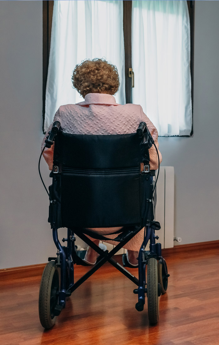 An elderly woman in a wheelchair alone in a nursing home room